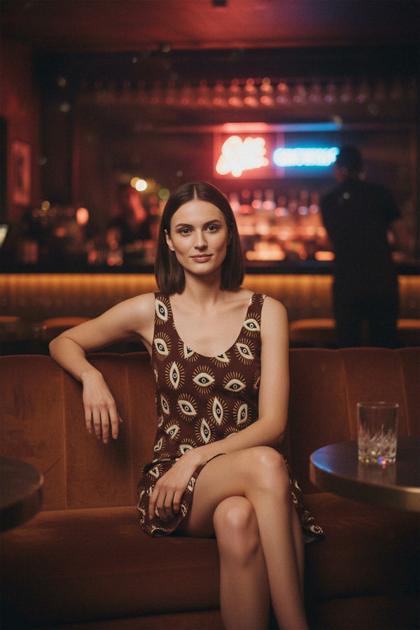 Chic evening outfit combining a brown eye print dress and maroon jacket in a bar interior.
